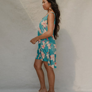 woman with brown hair wearing a teal v neck dress with ruffle hem and orchid pattern