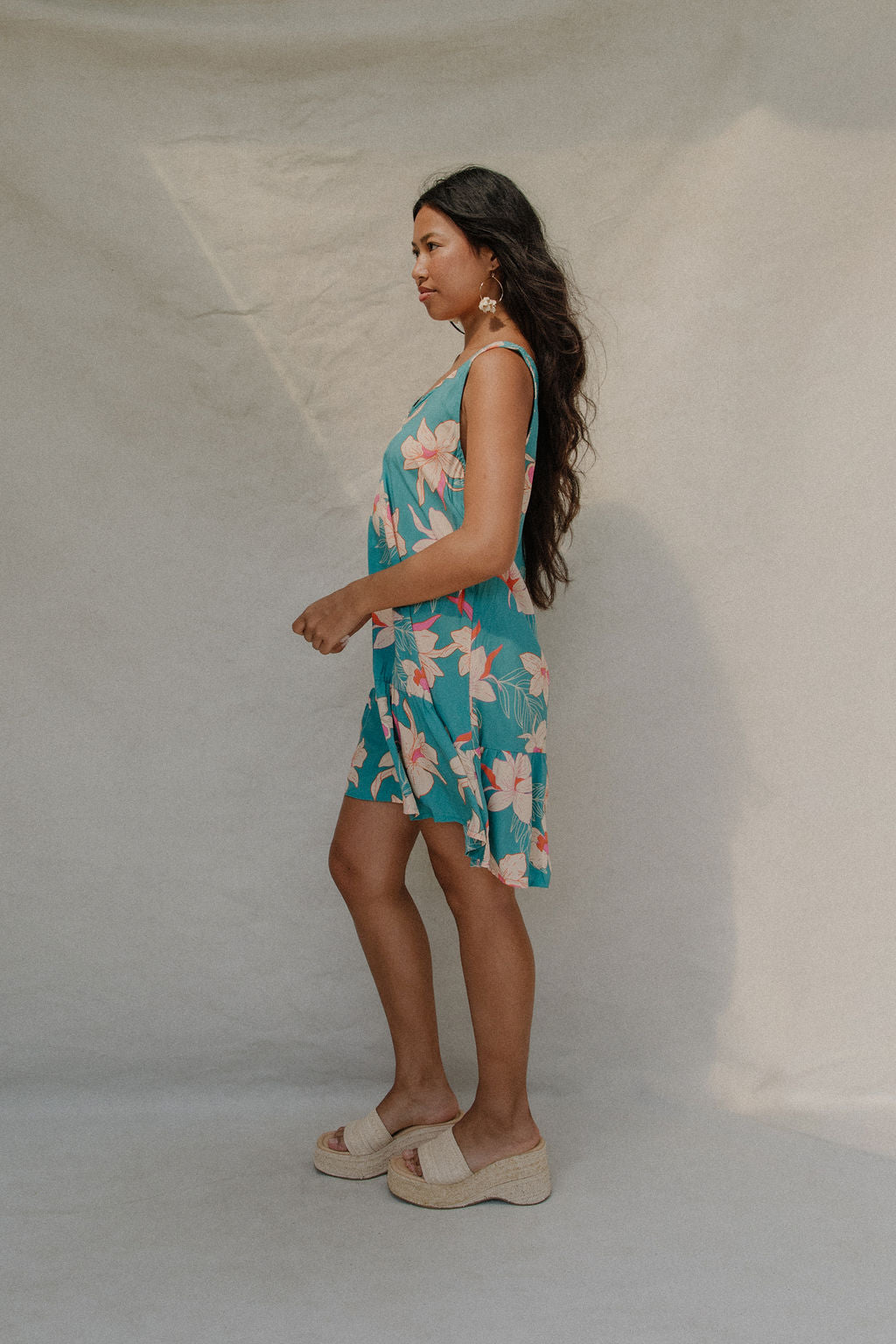 woman with brown hair wearing a teal v neck dress with ruffle hem and orchid pattern