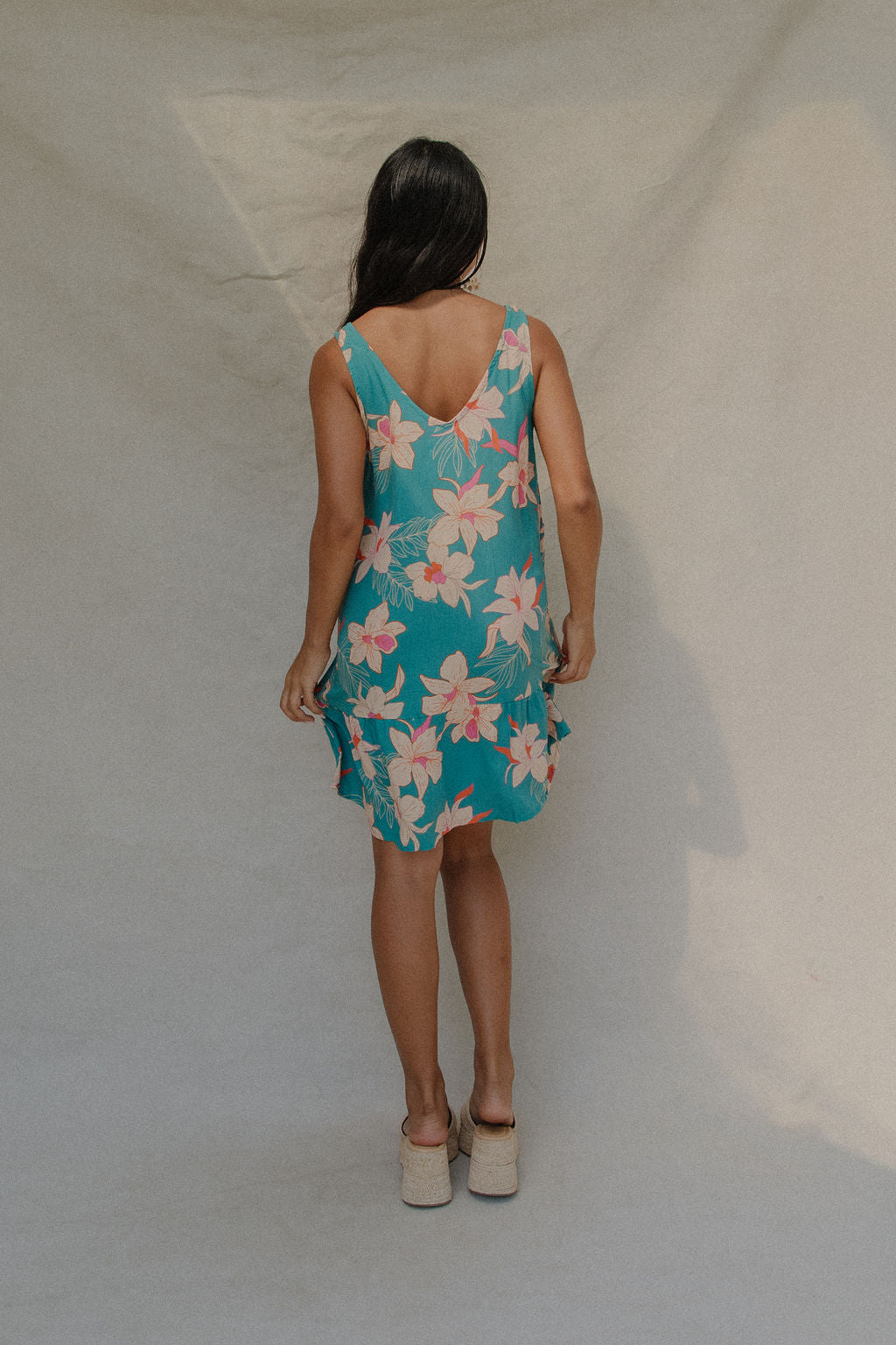 woman with brown hair wearing a teal v neck dress with ruffle hem and orchid pattern