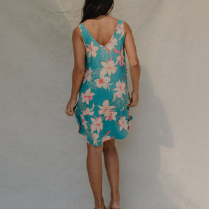 woman with brown hair wearing a teal v neck dress with ruffle hem and orchid pattern