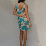 woman with brown hair wearing a teal v neck dress with ruffle hem and orchid pattern