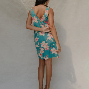 woman with brown hair wearing a teal v neck dress with ruffle hem and orchid pattern