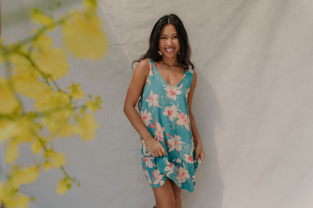 woman with brown hair wearing a teal v neck dress with ruffle hem and orchid pattern