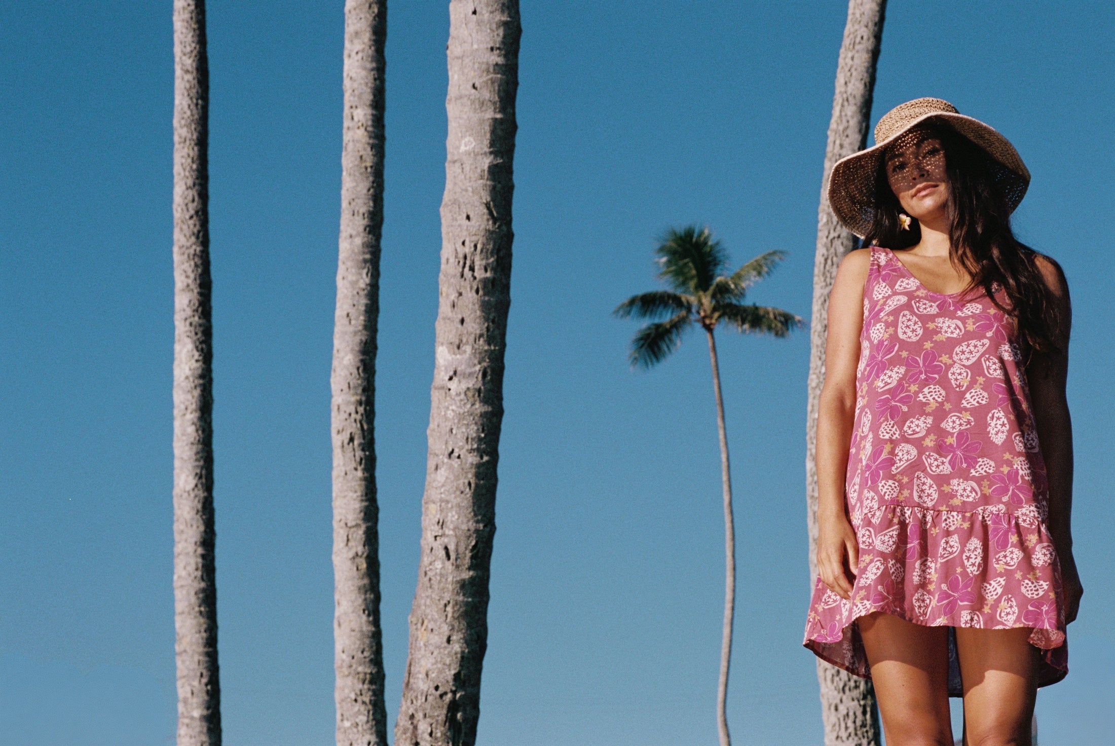 women with brown hair wearing a mini dress with shells and pua print in pink