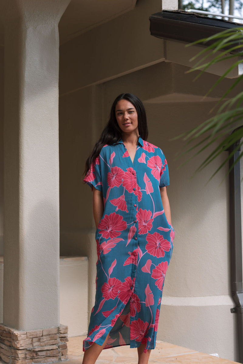 Woman wearing long blue dress with large pink and red floral print.