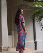 Woman wearing long blue dress with large pink and red floral print.