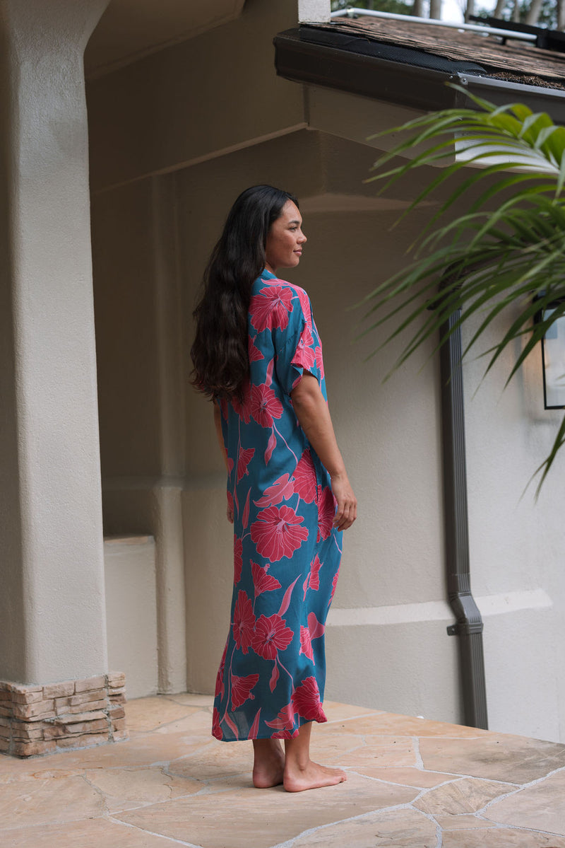 Woman wearing long blue dress with large pink and red floral print.