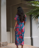 Woman wearing long blue dress with large pink and red floral print.