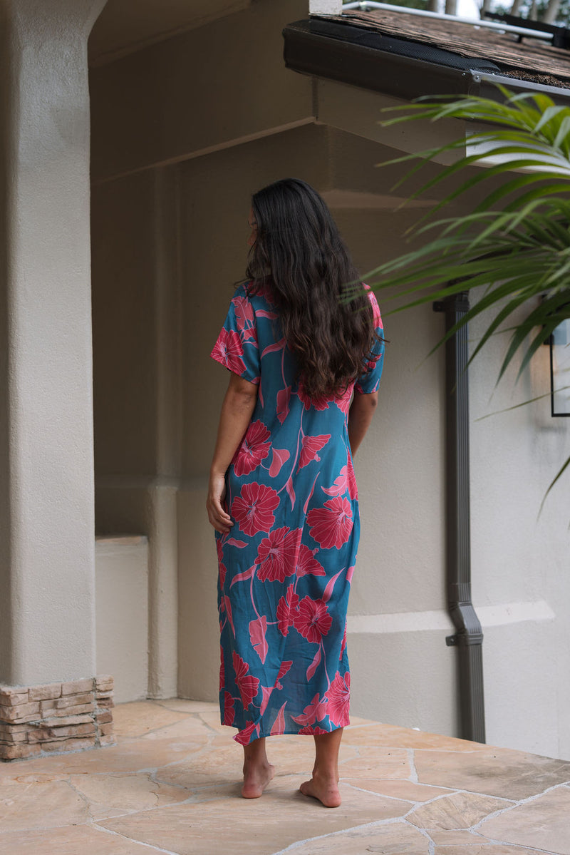 Woman wearing long blue dress with large pink and red floral print.