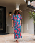 Woman wearing long blue dress with large pink and red floral print.