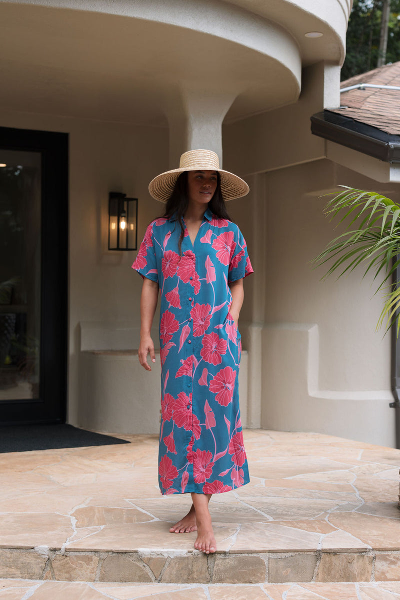 Woman wearing long blue dress with large pink and red floral print.