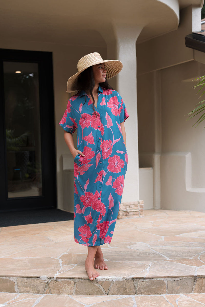 Woman wearing long blue dress with large pink and red floral print.