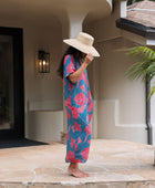 Woman wearing long blue dress with large pink and red floral print.