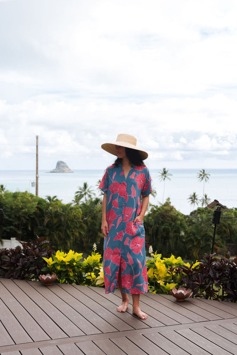 Woman wearing long blue dress with large pink and red floral print.