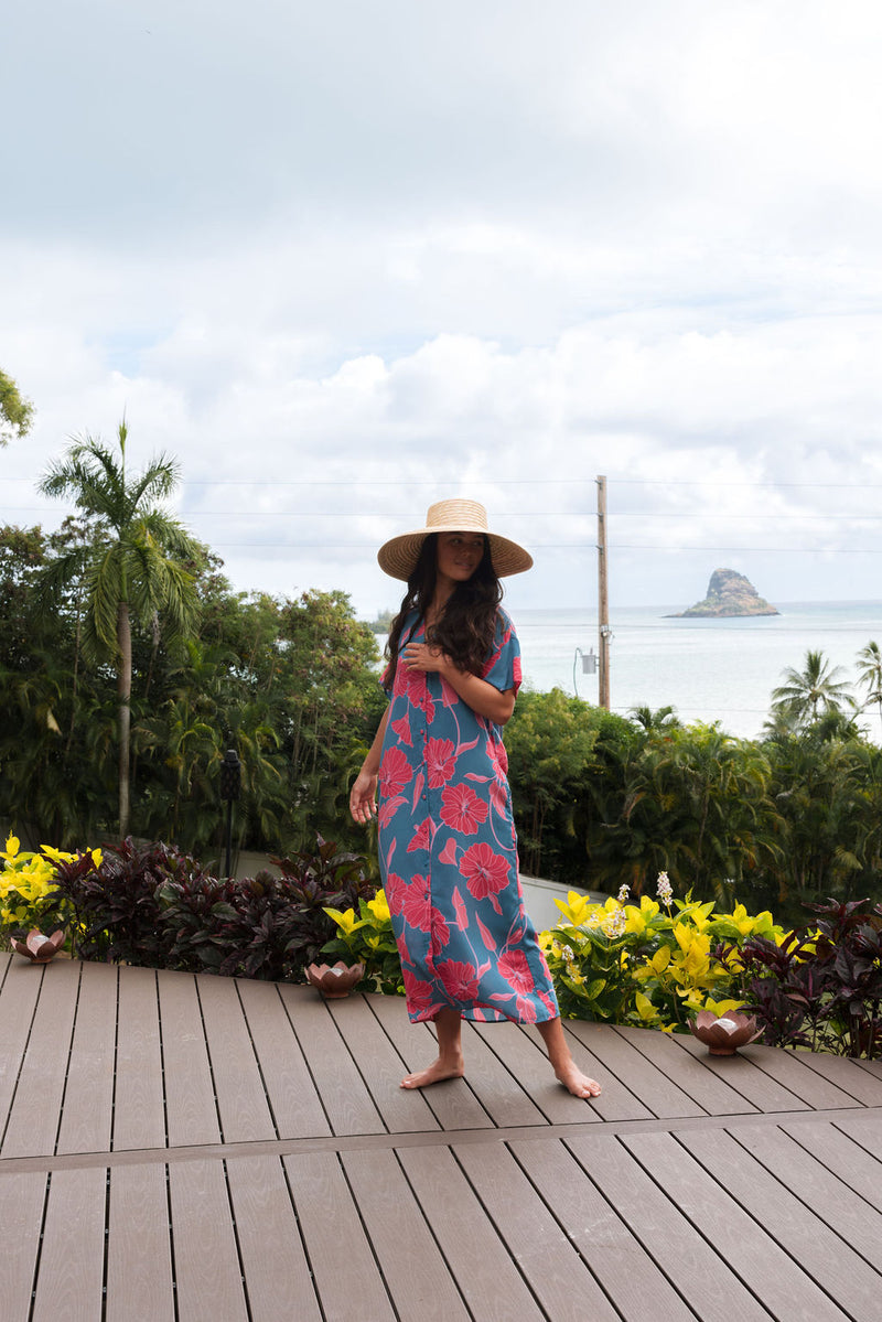 Woman wearing long blue dress with large pink and red floral print.