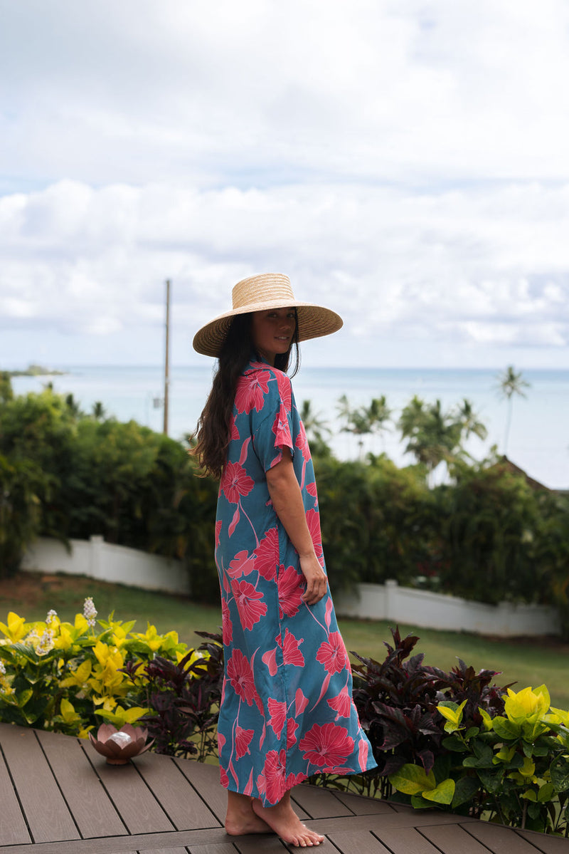 Woman wearing long blue dress with large pink and red floral print.