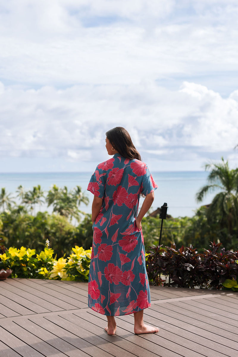 Woman wearing long blue dress with large pink and red floral print.