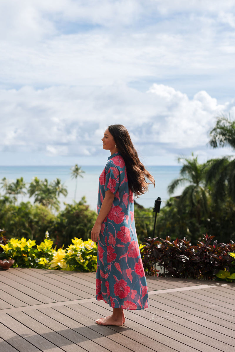 Woman wearing long blue dress with large pink and red floral print.