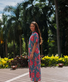 Woman wearing long blue dress with large pink and red floral print.