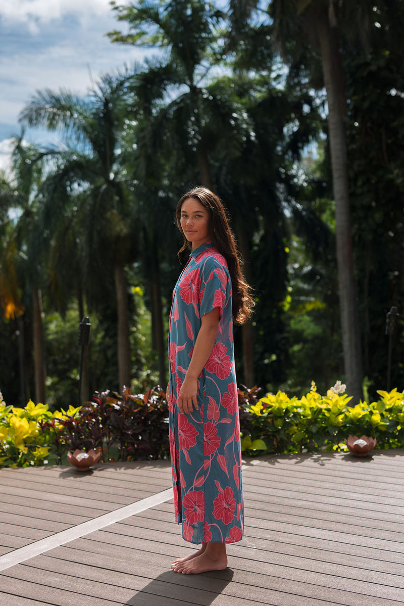 Woman wearing long blue dress with large pink and red floral print.