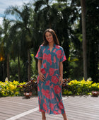 Woman wearing long blue dress with large pink and red floral print.