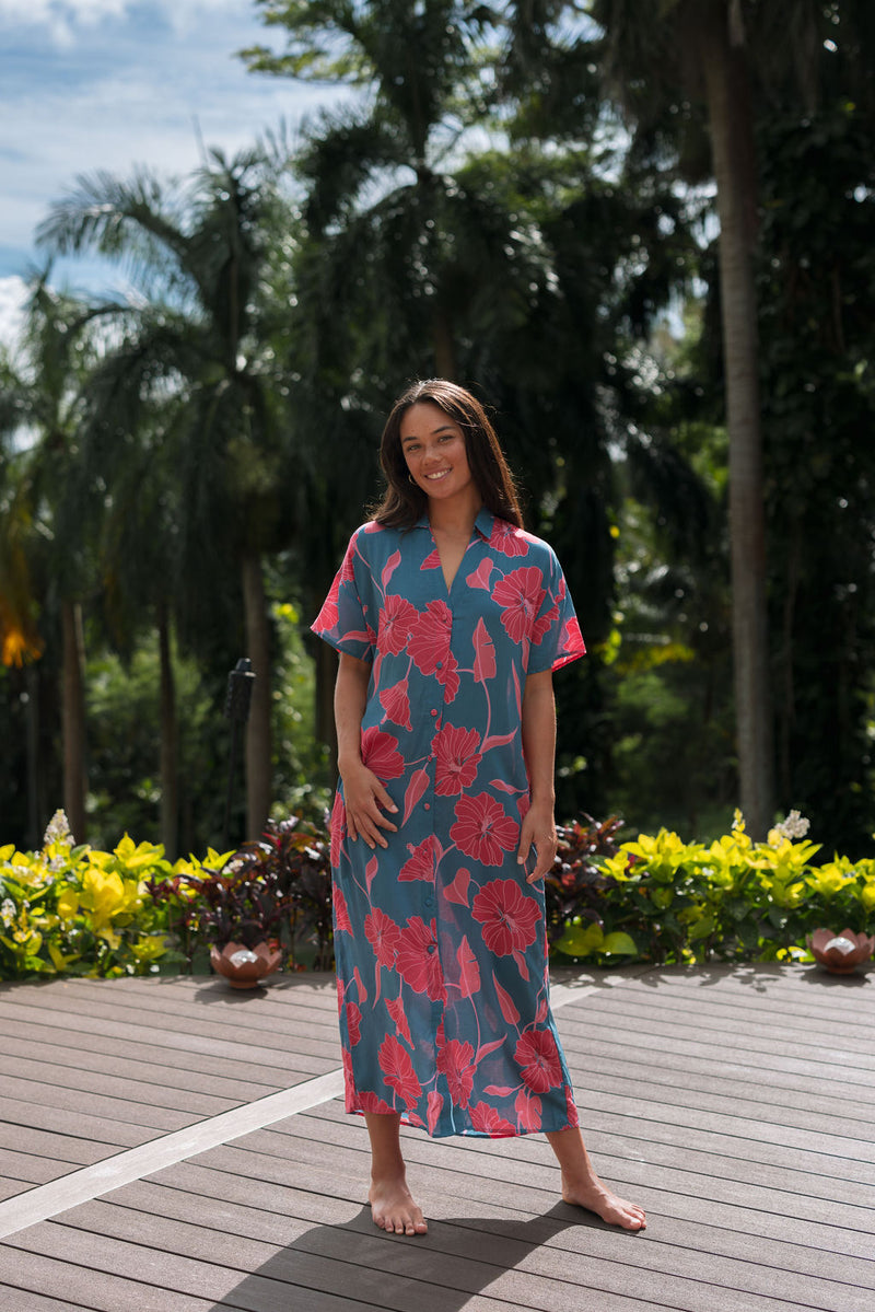 Woman wearing long blue dress with large pink and red floral print.