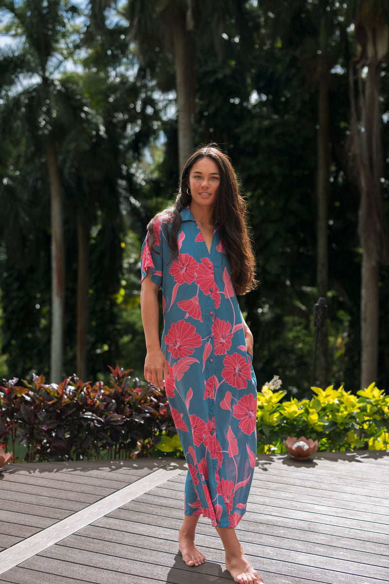 Woman wearing long blue dress with large pink and red floral print.