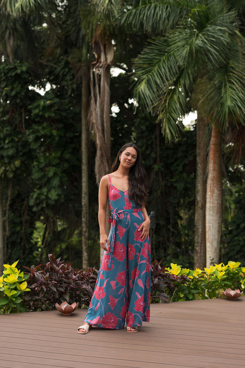 Woman wearing long blue sleeveless jumpsuit with large pink and red floral print.