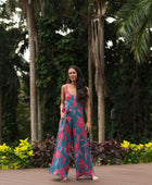 Woman wearing long blue sleeveless jumpsuit with large pink and red floral print.