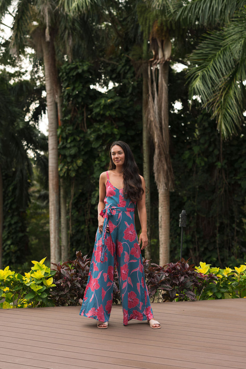 Woman wearing long blue sleeveless jumpsuit with large pink and red floral print.