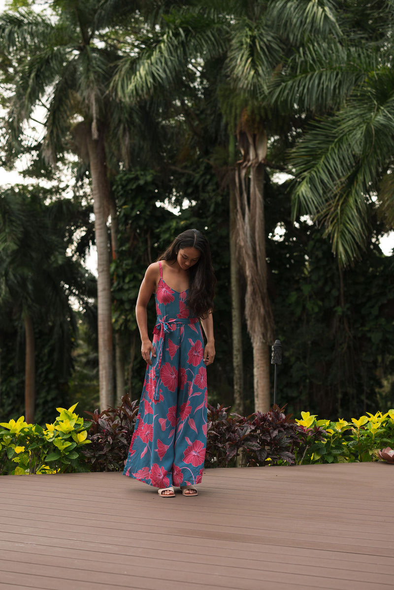 Woman wearing long blue sleeveless jumpsuit with large pink and red floral print.