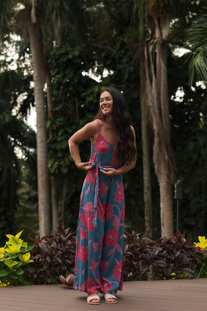 Woman wearing long blue sleeveless jumpsuit with large pink and red floral print.