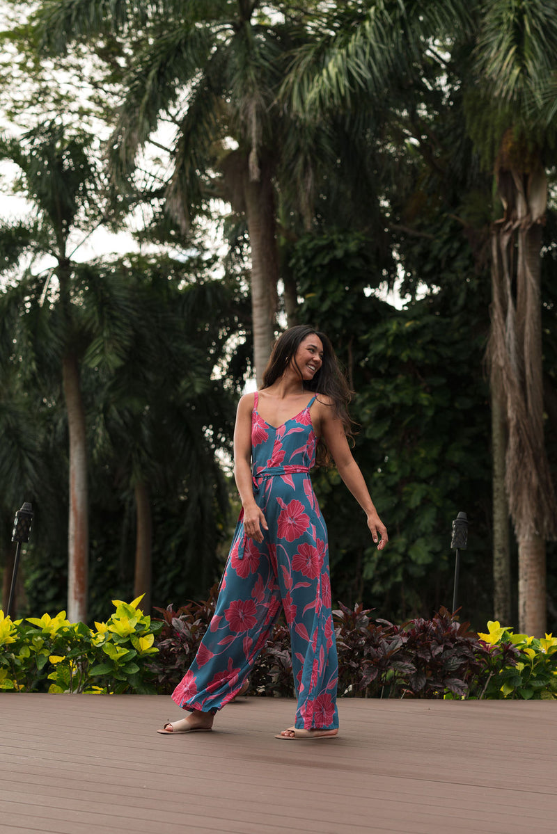 Woman wearing long blue sleeveless jumpsuit with large pink and red floral print.