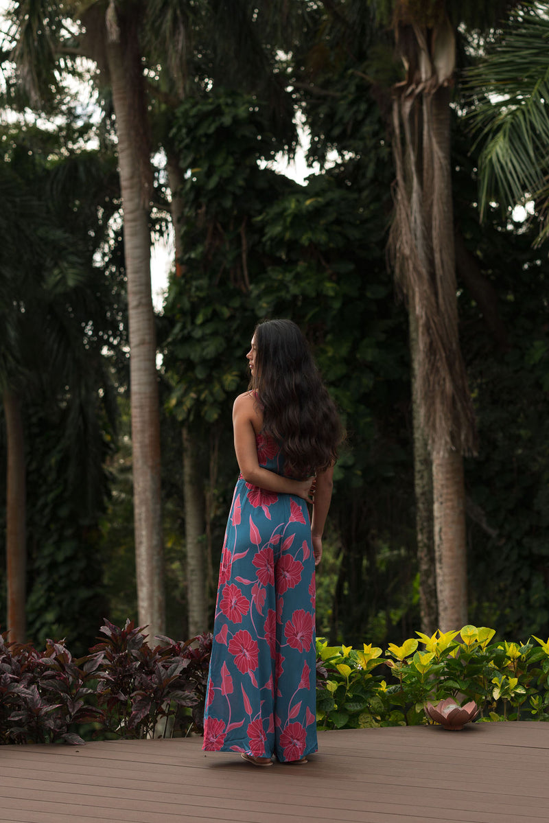 Woman wearing long blue sleeveless jumpsuit with large pink and red floral print.