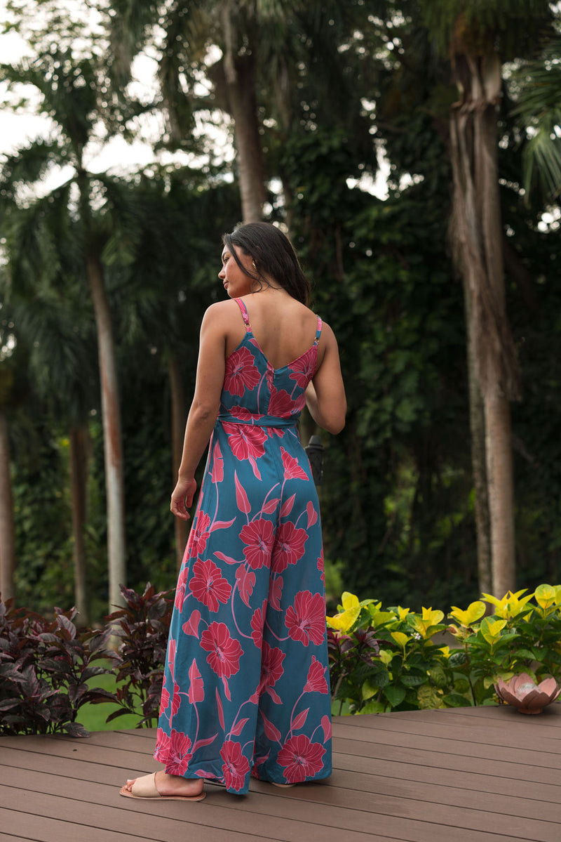 Woman wearing long blue sleeveless jumpsuit with large pink and red floral print.