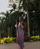 Woman wearing long blue sleeveless jumpsuit with large pink and red floral print.