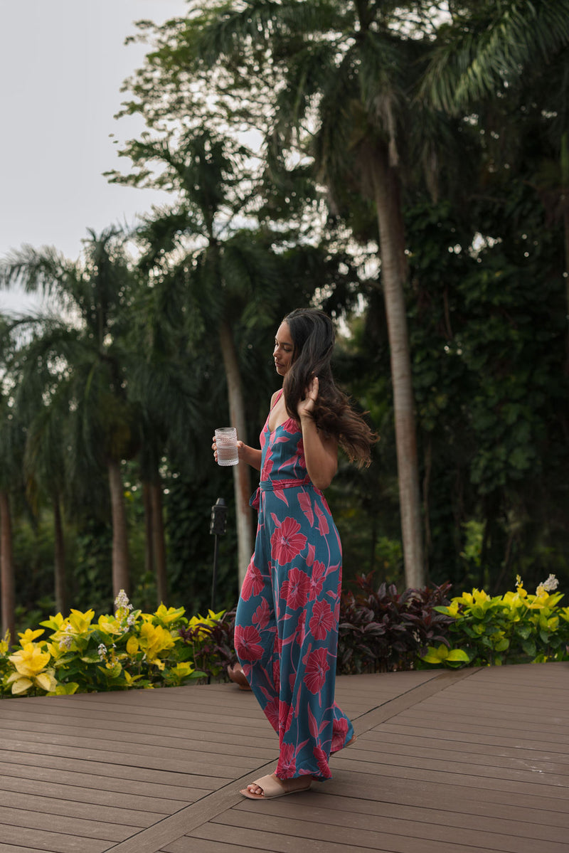 Woman wearing long blue sleeveless jumpsuit with large pink and red floral print.