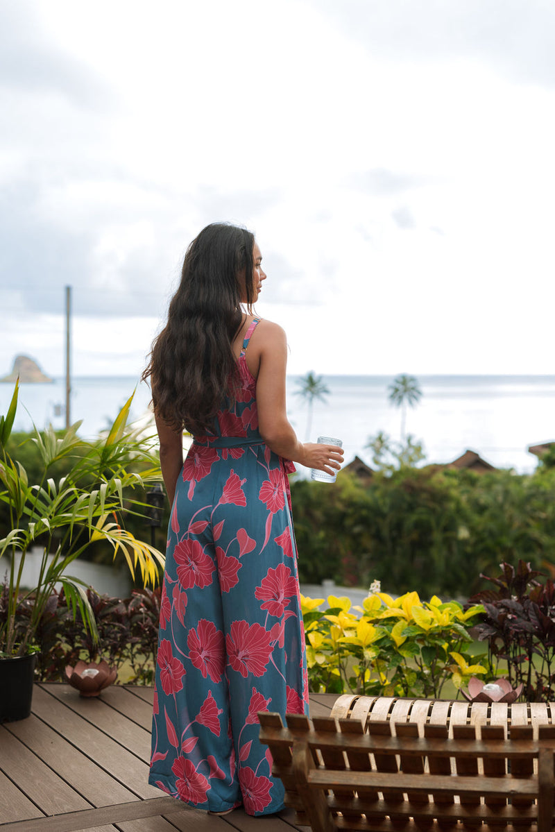 Woman wearing long blue sleeveless jumpsuit with large pink and red floral print.