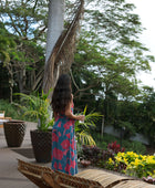 Woman wearing long blue sleeveless jumpsuit with large pink and red floral print.