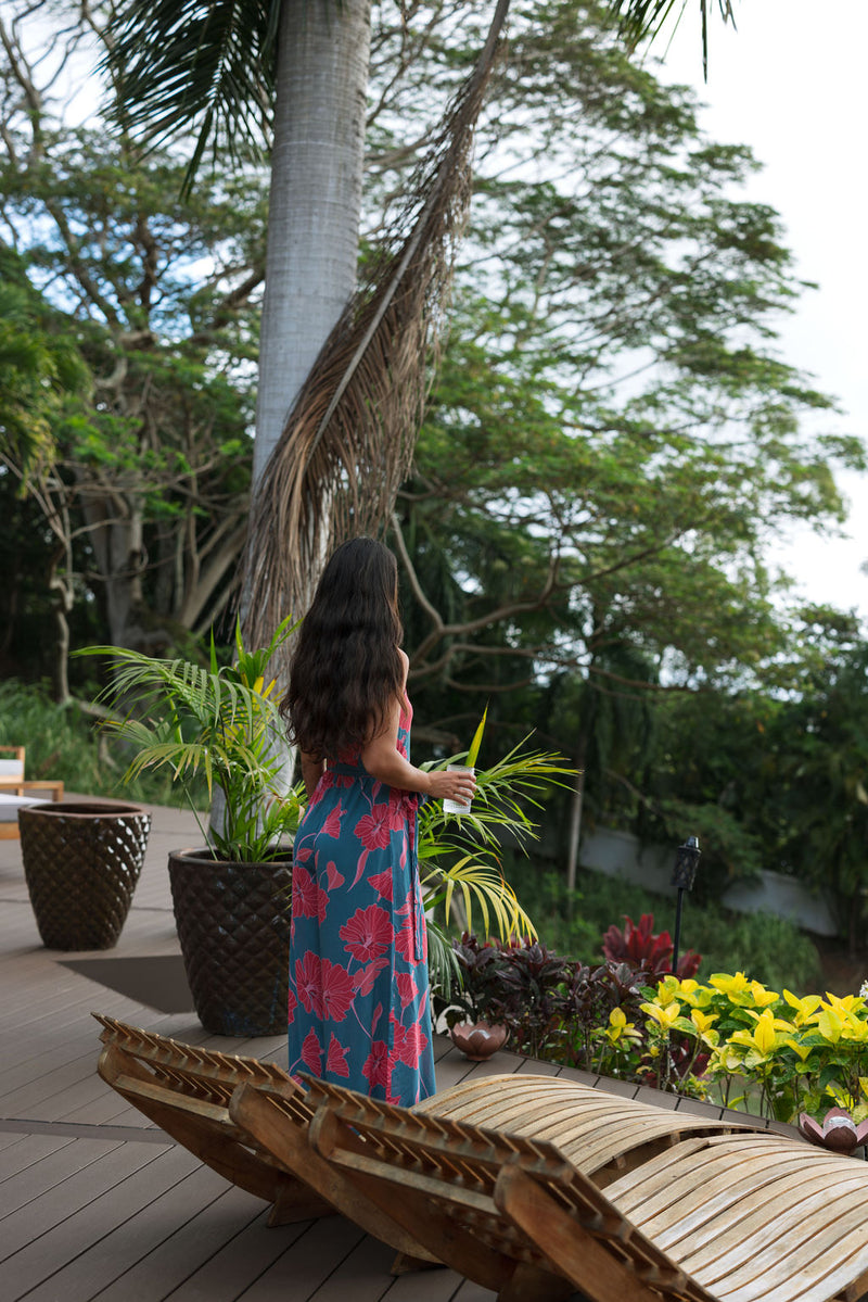 Woman wearing long blue sleeveless jumpsuit with large pink and red floral print.