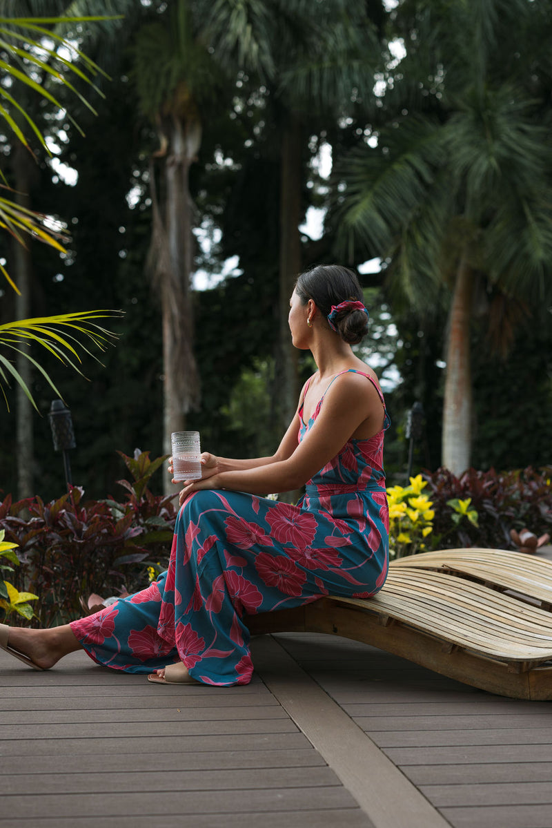 Woman wearing long blue sleeveless jumpsuit with large pink and red floral print.