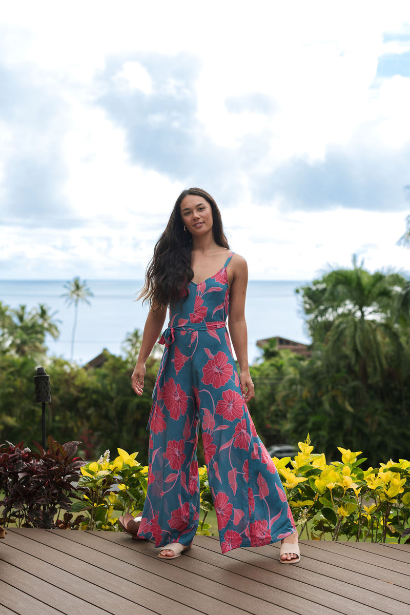 Woman wearing long blue sleeveless jumpsuit with large pink and red floral print.