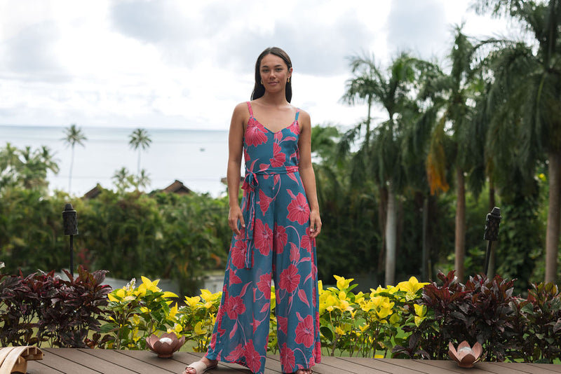 Woman wearing long blue sleeveless jumpsuit with large pink and red floral print.