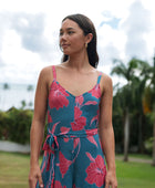 Woman wearing long blue sleeveless jumpsuit with large pink and red floral print.