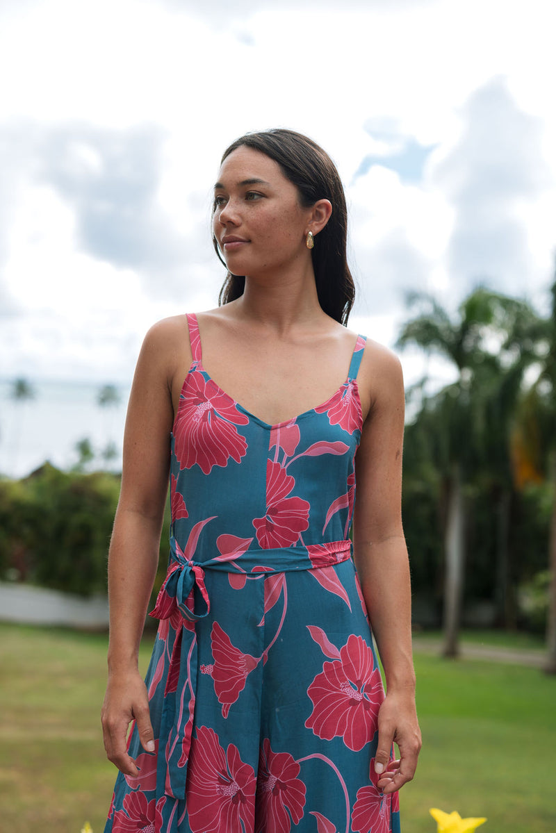 Woman wearing long blue sleeveless jumpsuit with large pink and red floral print.