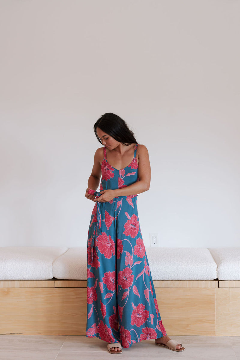 Woman wearing long blue sleeveless jumpsuit with large pink and red floral print.