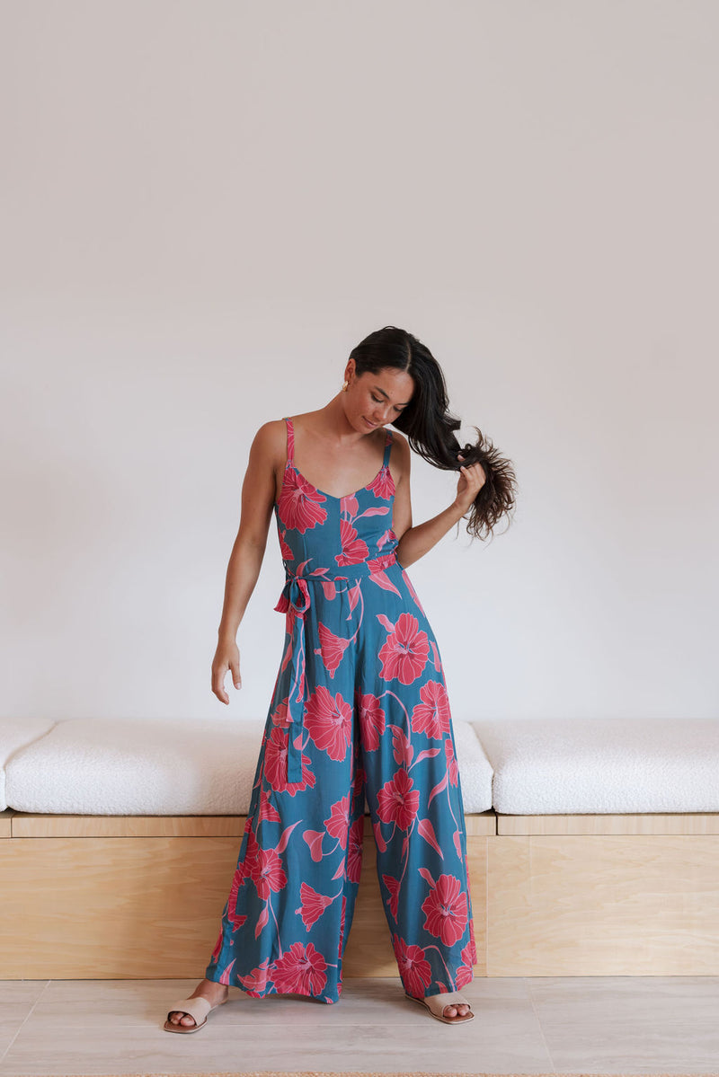 Woman wearing long blue sleeveless jumpsuit with large pink and red floral print.