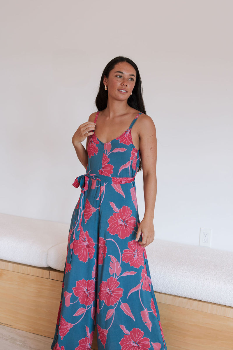 Woman wearing long blue sleeveless jumpsuit with large pink and red floral print.