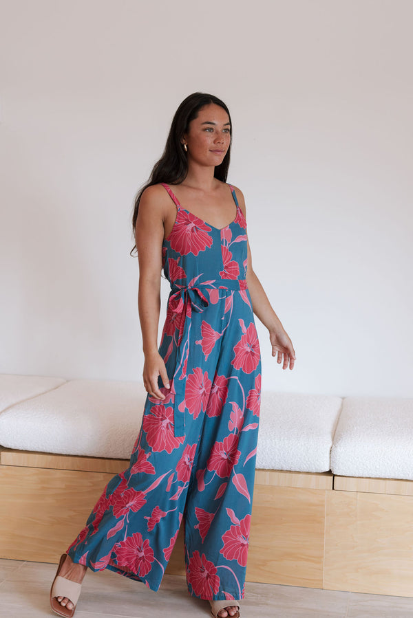 Woman wearing long blue sleeveless jumpsuit with large pink and red floral print.