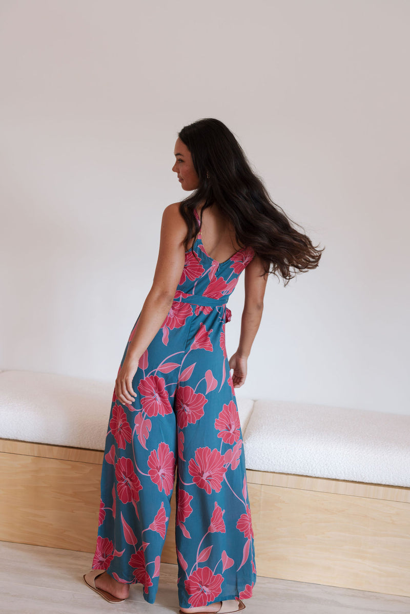 Woman wearing long blue sleeveless jumpsuit with large pink and red floral print.